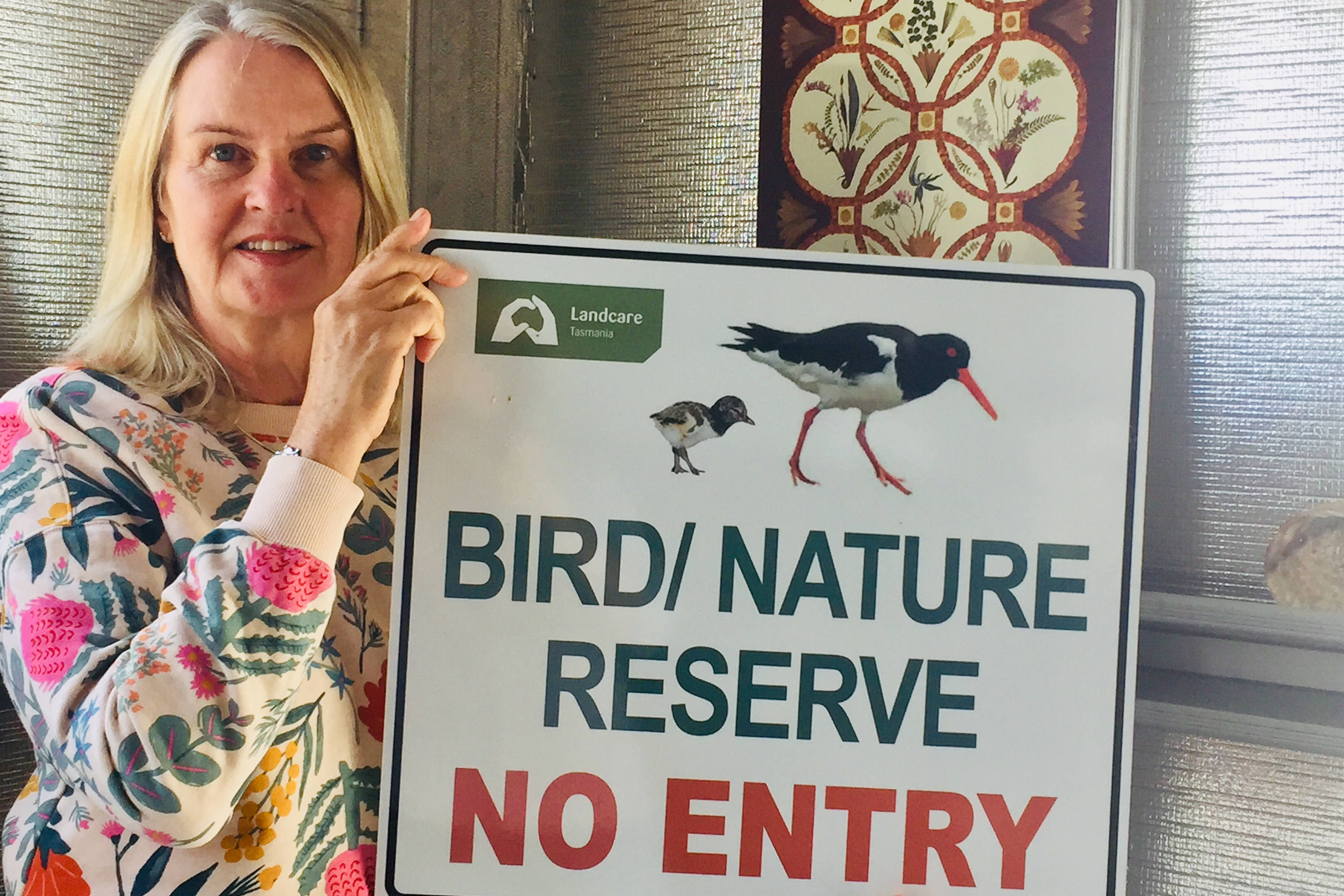 Robyn Lewis, this month’s Climate Champ, holding sign that says ‘BIRD/NATURE RESERVE NO ENTRY’. Photo: Lian Tanner.